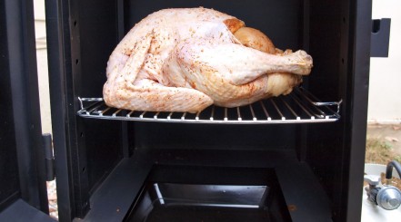A chicken on the top shelf of an open propane gas smoker