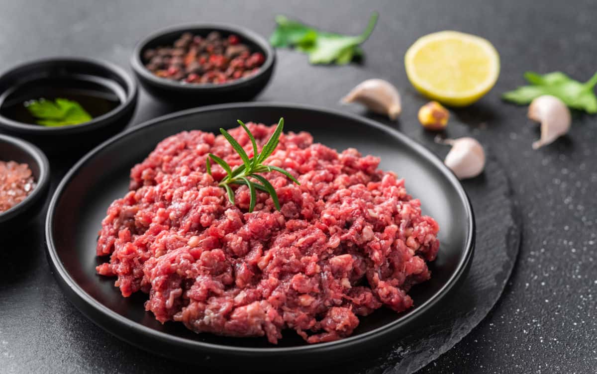 Ground meat with a sprig of rosemary, in a dark bowl, on a dark surface