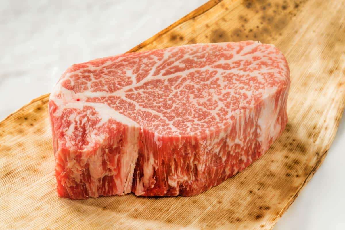 A 2 inch thick wagyu cross steak with intense marbling, on a cutting board on white backgro.