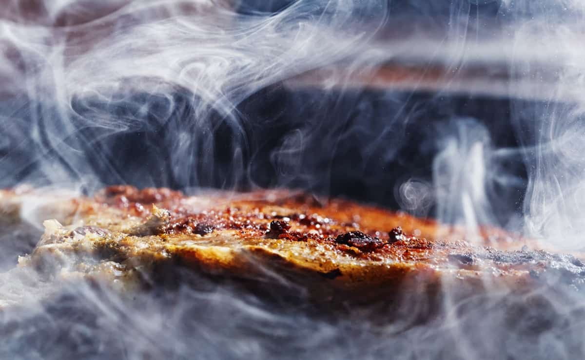 A small cut of pork being enveloped with rolling smoke