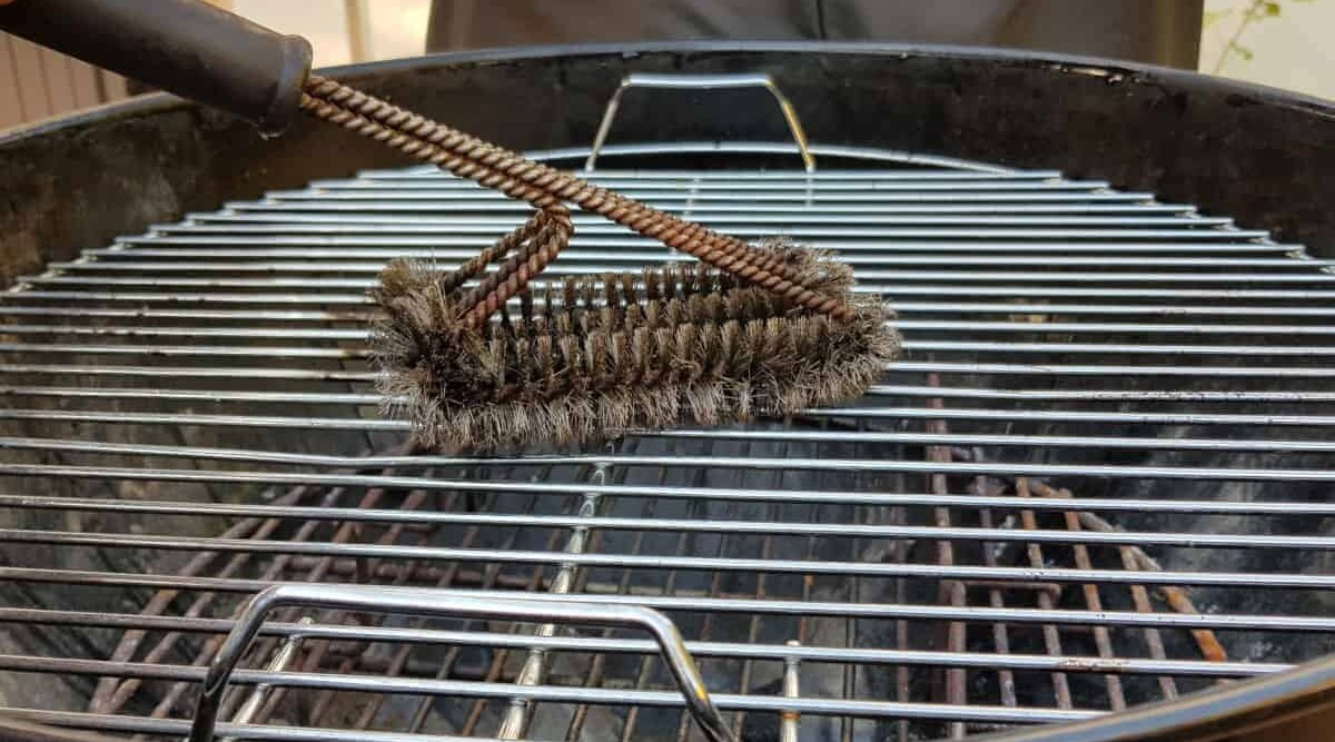 Stainless steel grill grates being cleaned with a wire brush.