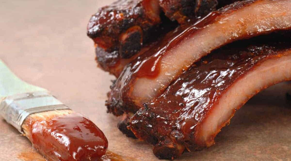 BBQ ribs dripping in thick sauce with a paint brush laying beside them.