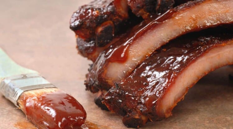 BBQ ribs dripping in thick sauce with a paint brush laying beside them.