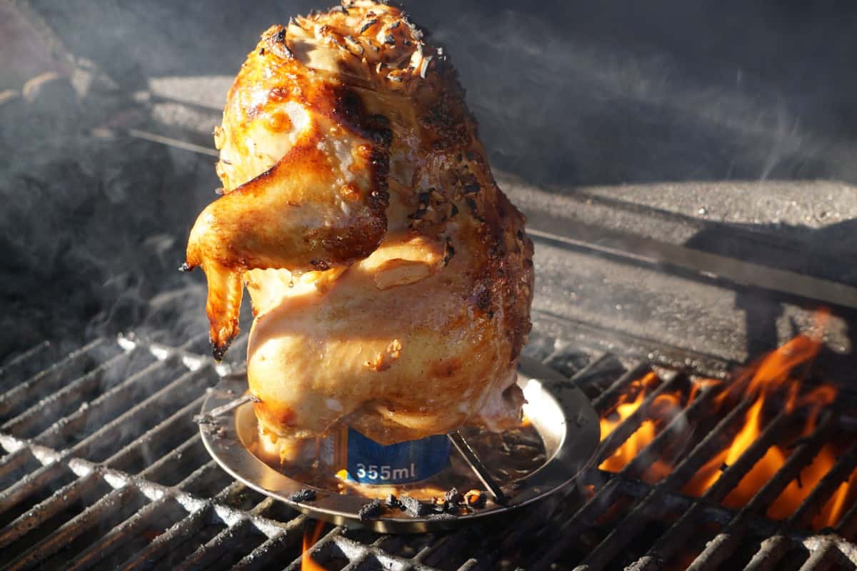 A whole chicken sitting on a beer can, roasting in a charcoal grill