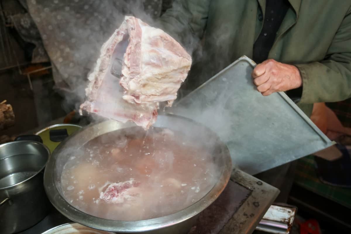 A man boiling pork ribs in a large aluminum pan