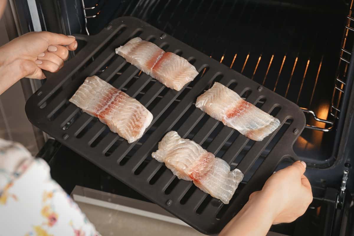 A broiler pan of fish fillets going into a broiler o.