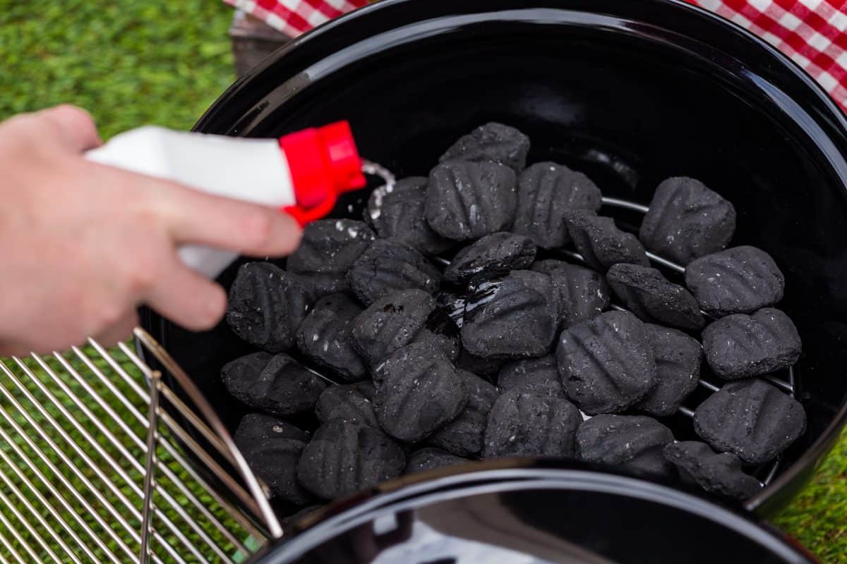 Lighter fluid being poured onto charcoal briquettes in a gr.