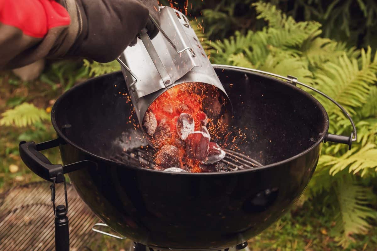 A man pouring lit coals from a chimney starter into a charcoal gr.