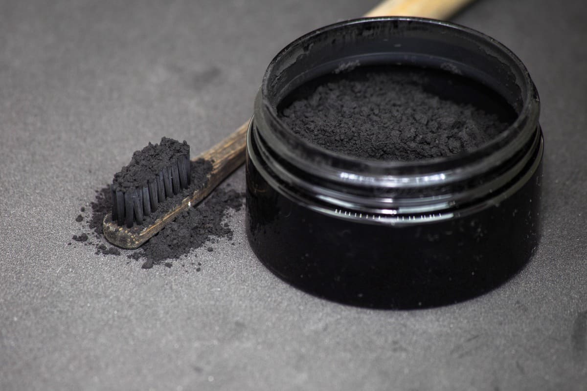 charcoal toothpaste in a small pot, and on a toothbrushes brist.