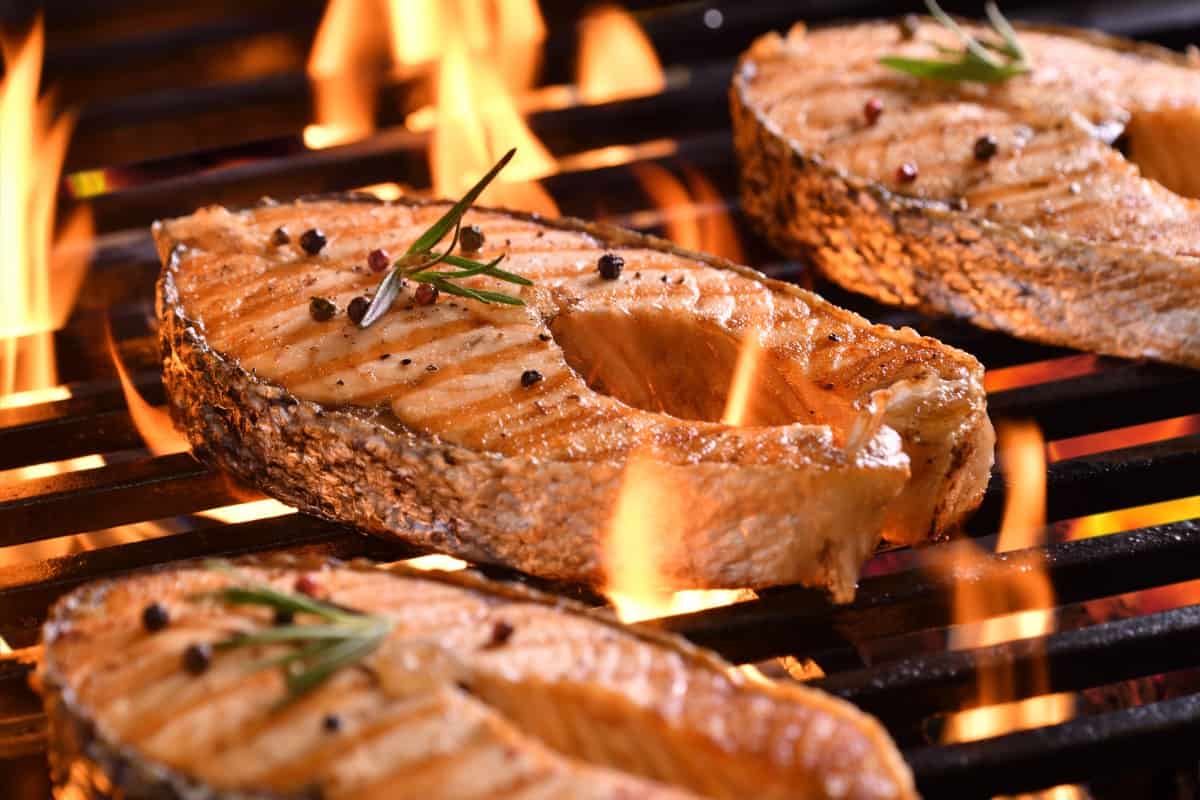 Salmon steaks being grilled on cast iron grates over hot fla.