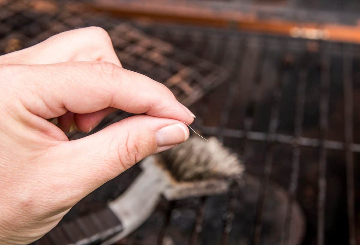 A persons hand holding a wire bristle from a grill br.