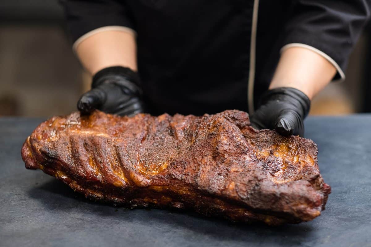 A mans black gloved hands holding some smoked pork r.