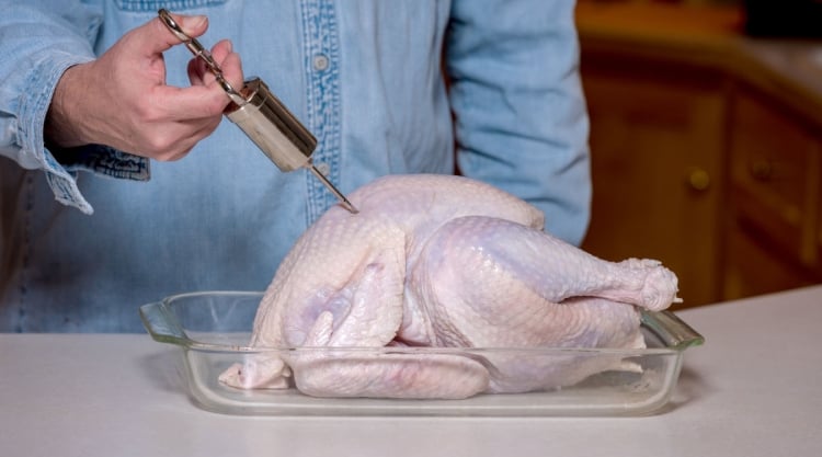 A turkey being injected with marinade by a man in a blue shirt.