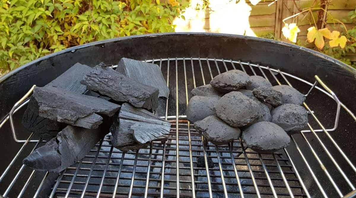 A close up of unlit lump charcoal next to briquettes on a weber grill.