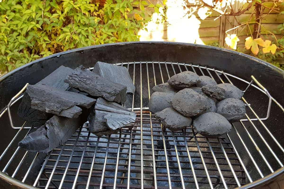 A close up of unlit lump charcoal next to briquettes on a weber gr.