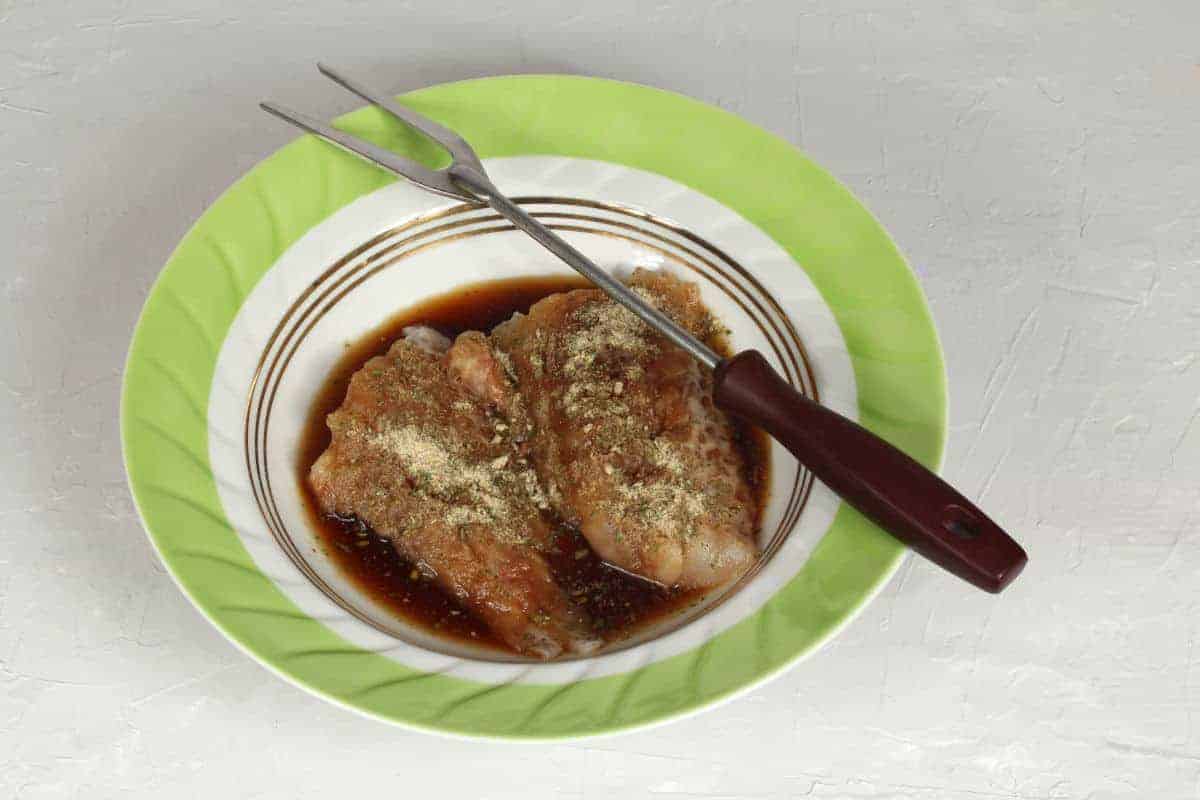 Some meat marinading in a bowl with a fork resting on the e.