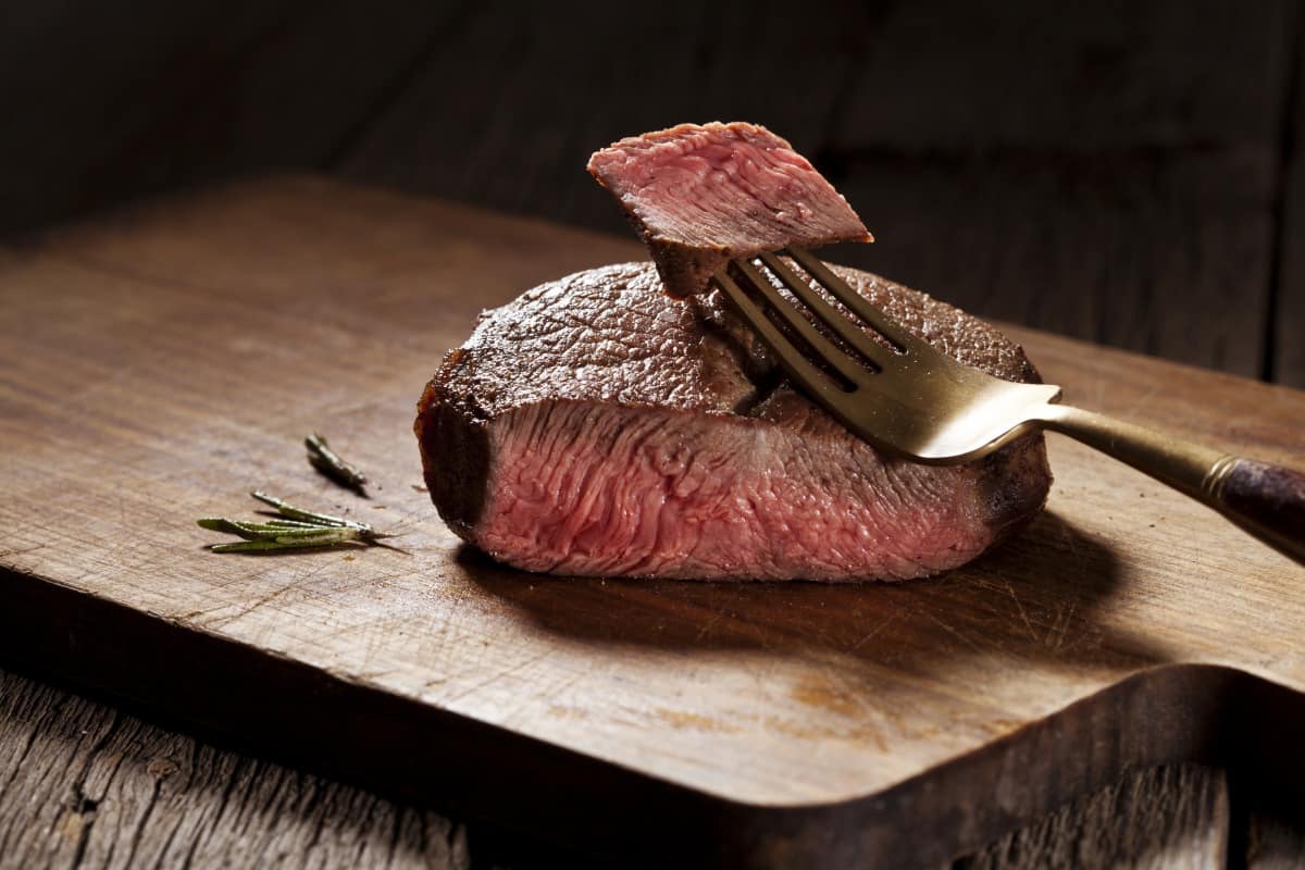 A rare filet steak, slice in half with a small piece on a fork showing how pink it.