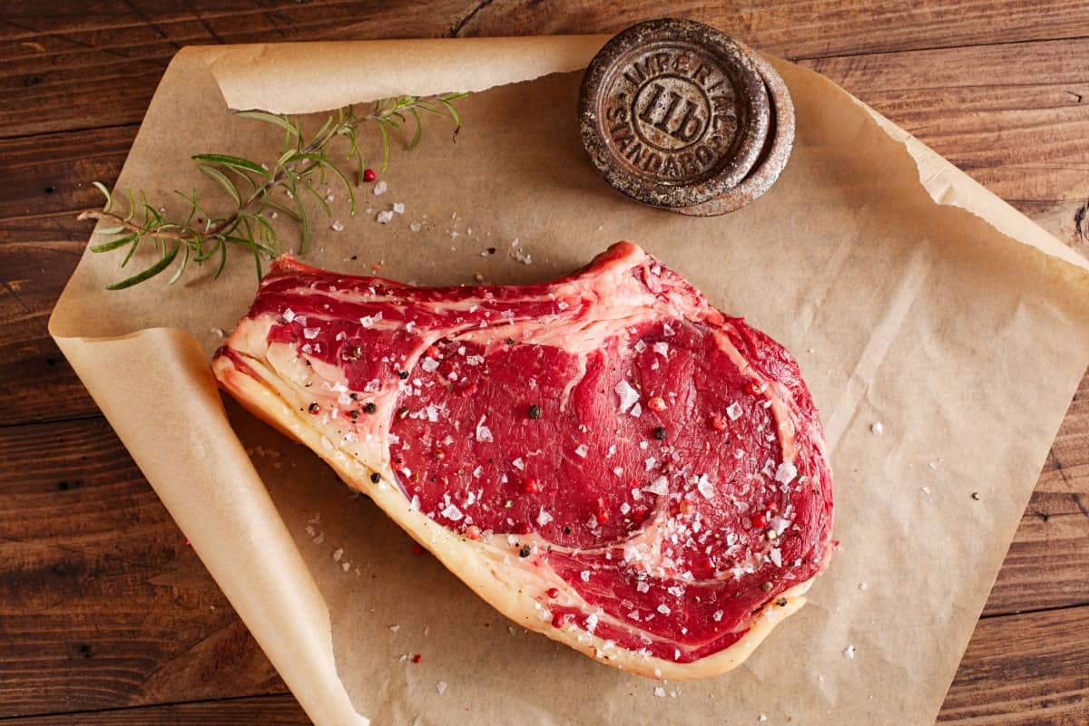 A raw rib steak on butcher paper, with a weight holding the paper o.