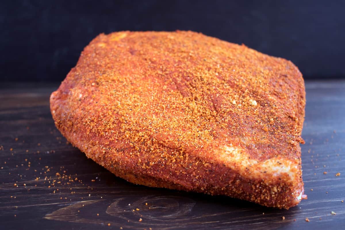 Brisket rubbed in a brown colored dry spice mix, ready for smoking