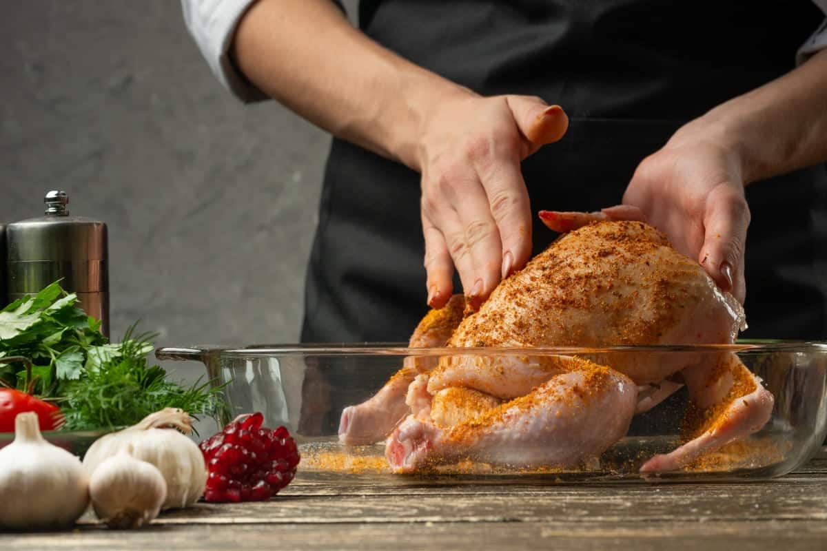 A chef rubbing a chicken, with some garlic and herbs in the forefront of the photo