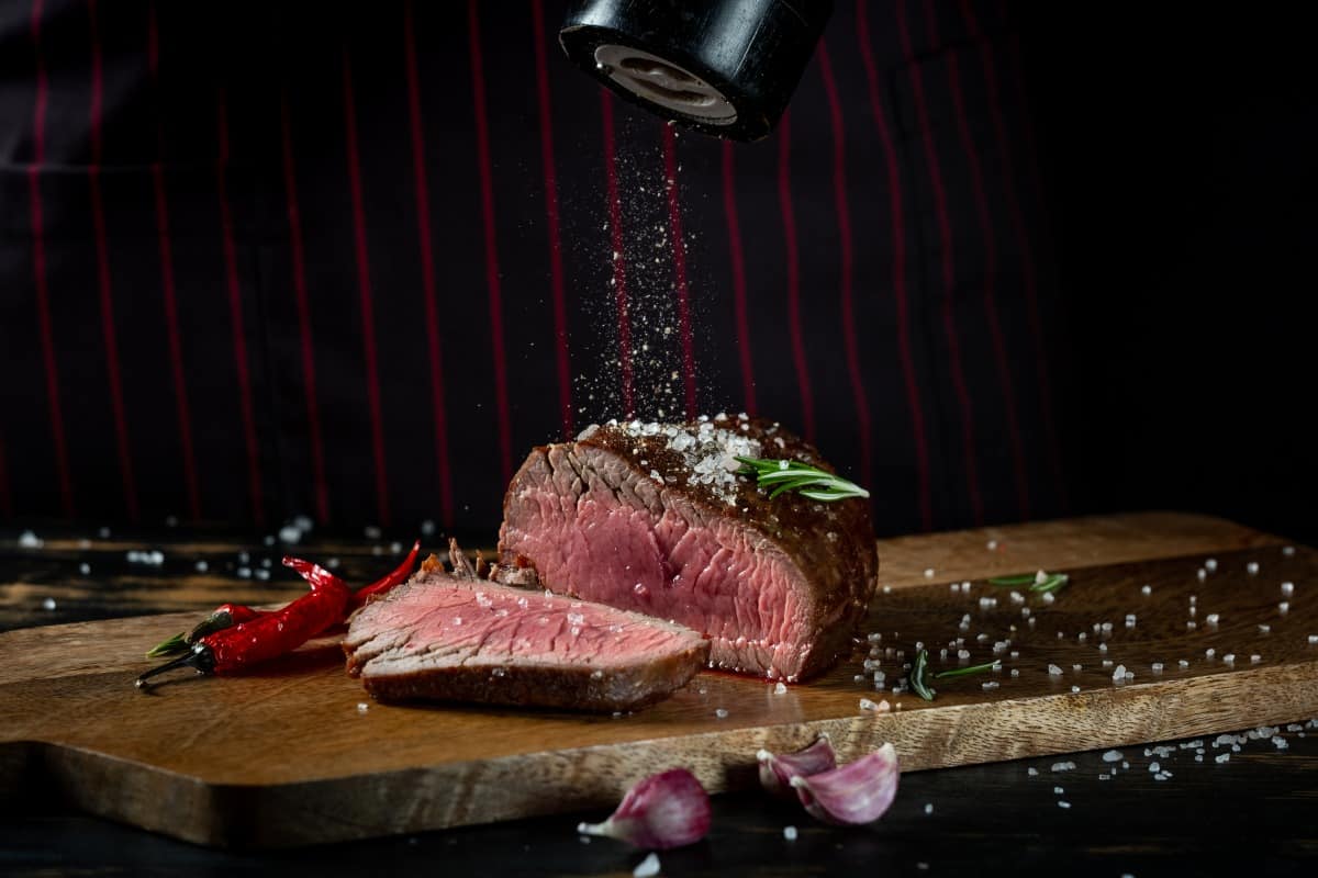 Salt being sprinkled onto a grilled filet mignon steak sliced in half, showing it's insides cooked to r.