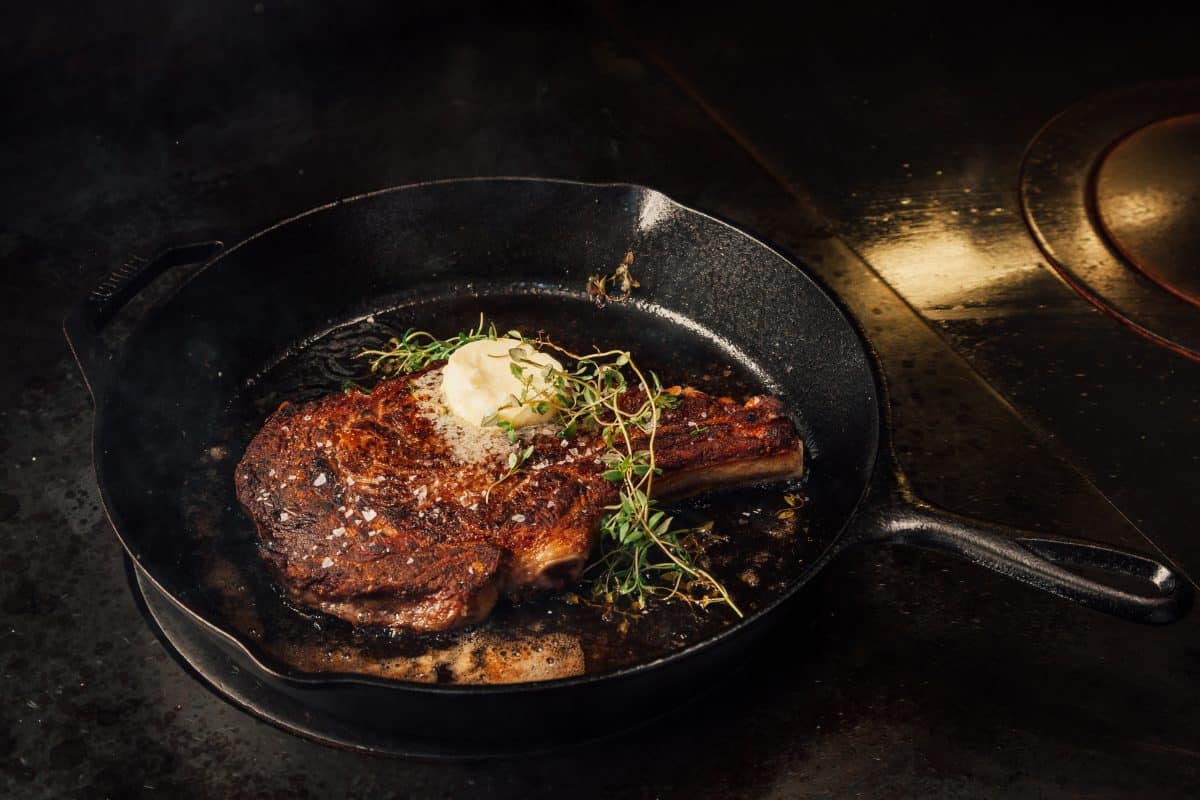 Steak searing in a pan, with butter melting on top and some thyme placed in the .