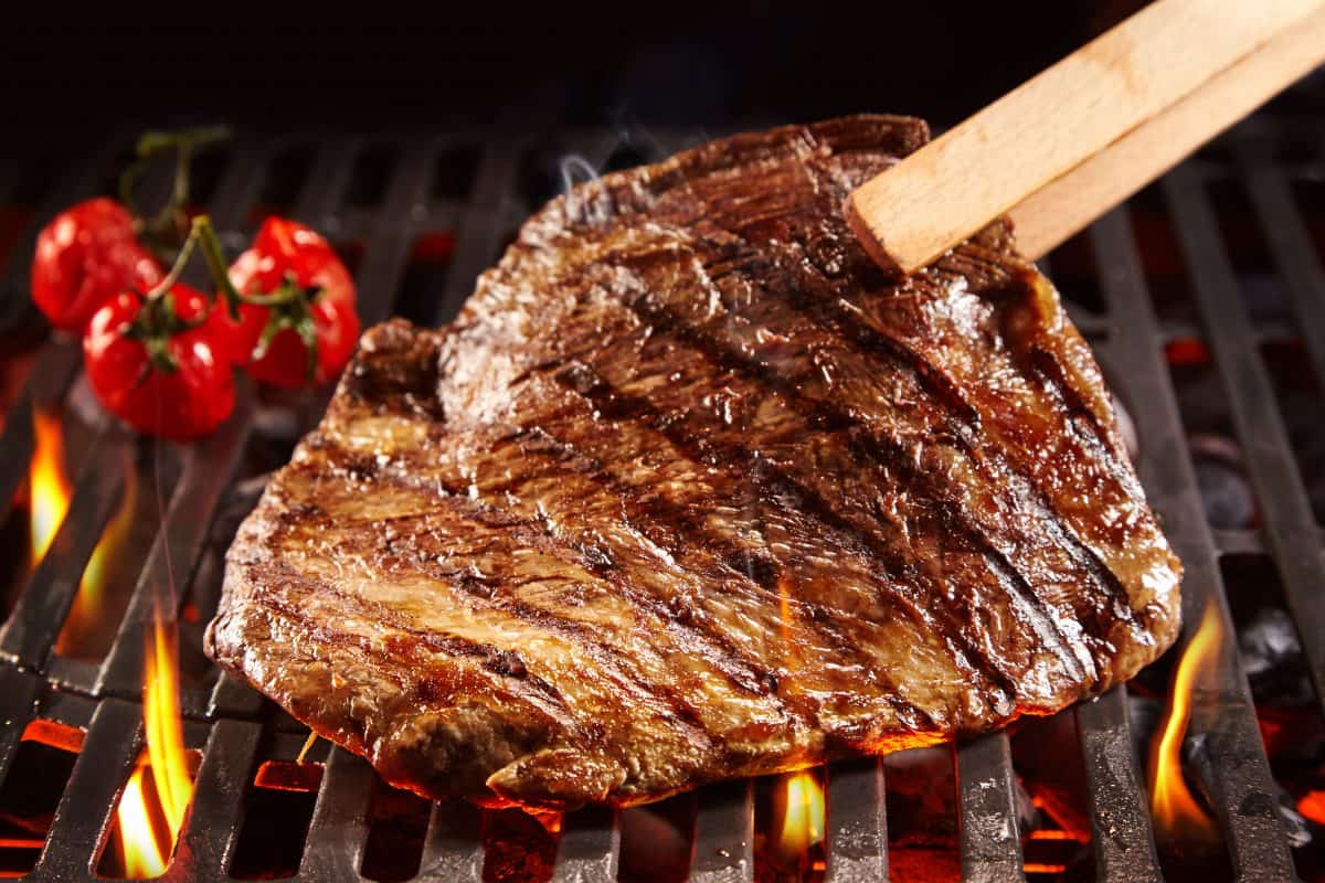 Meat held between wooden tongs, being picked up from being seared on a flaming gr.