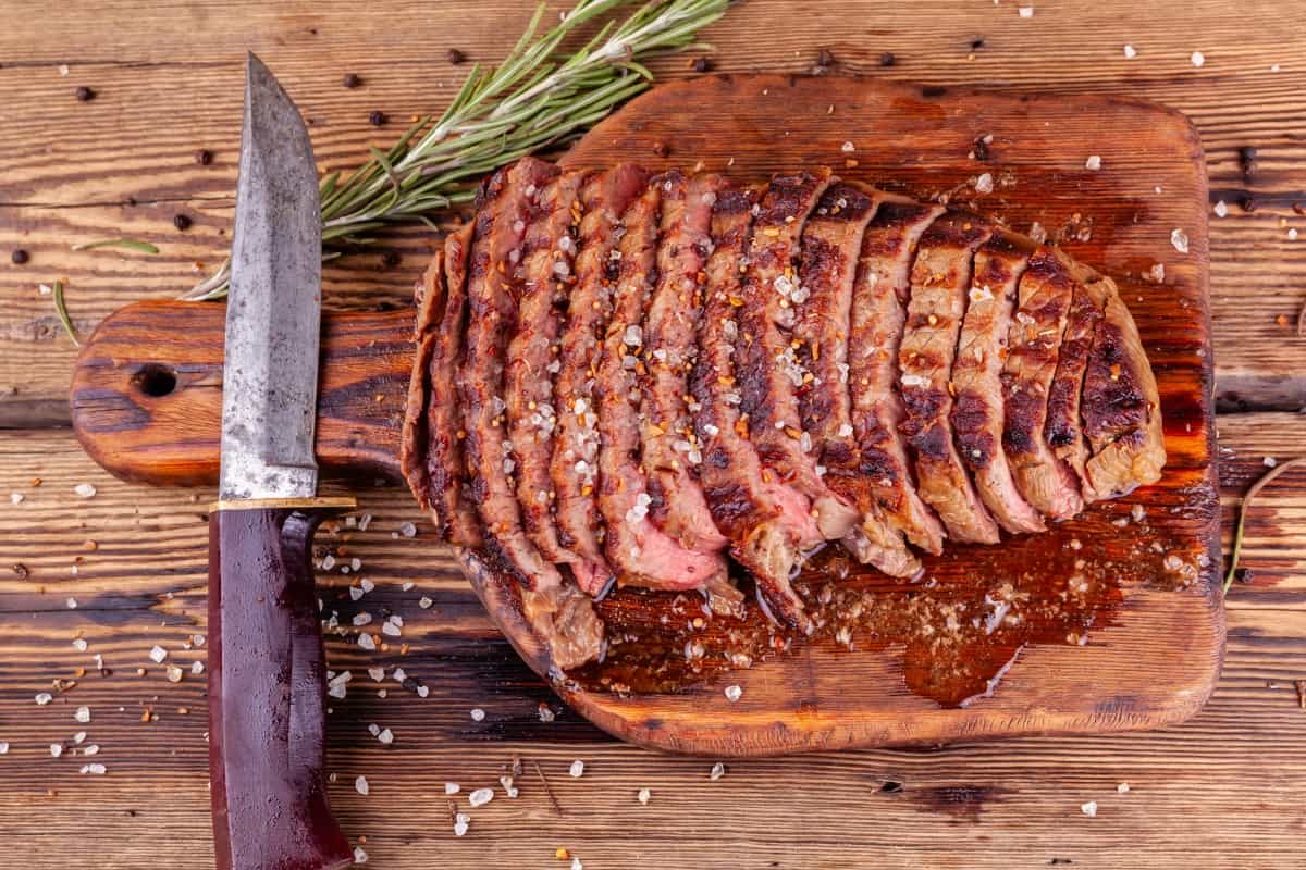 sliced beef leaking juices on a cutting board, next to a steak kn.