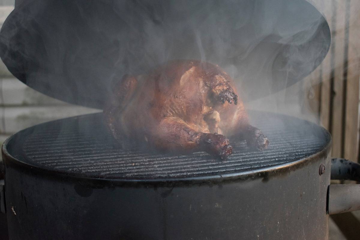 A water smoker with lid lifted, showing a chicken being smo.