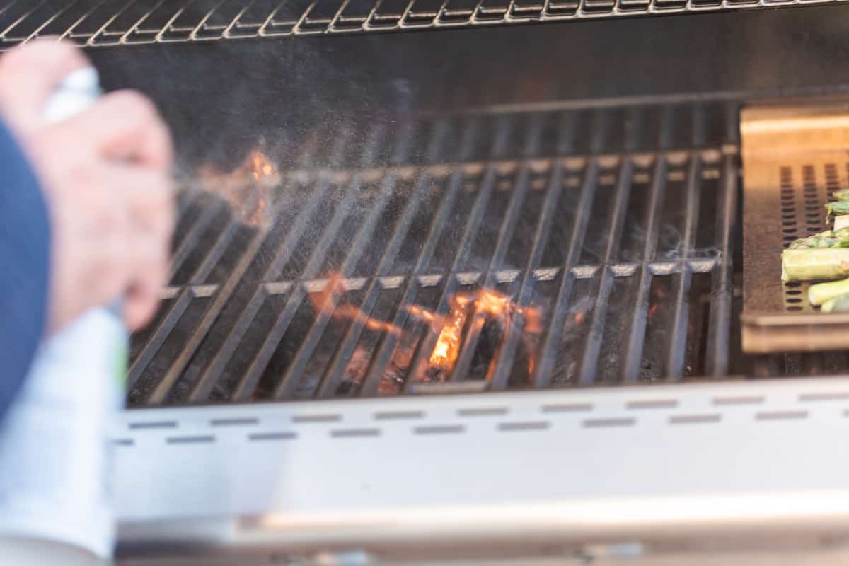 A spray bottle of water being used to put out the flames of a grill flare.
