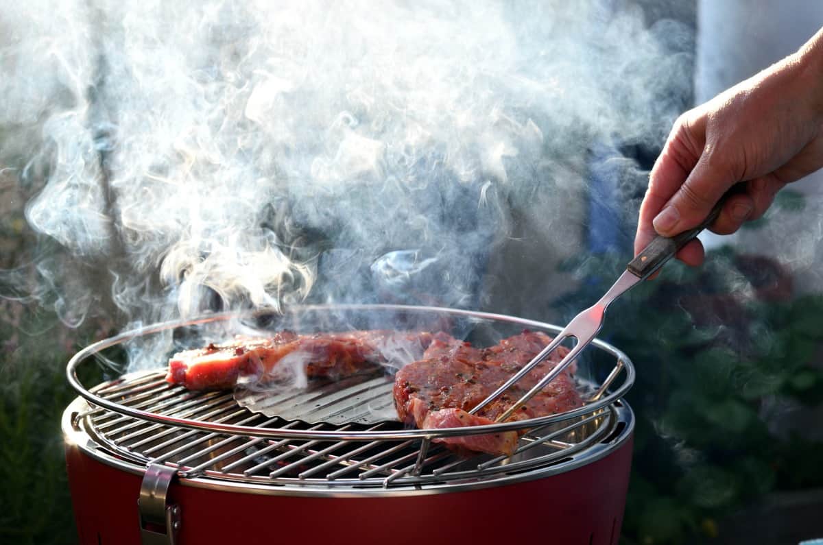 A man turning meat with a BBQ fork on a small, round, smoking .