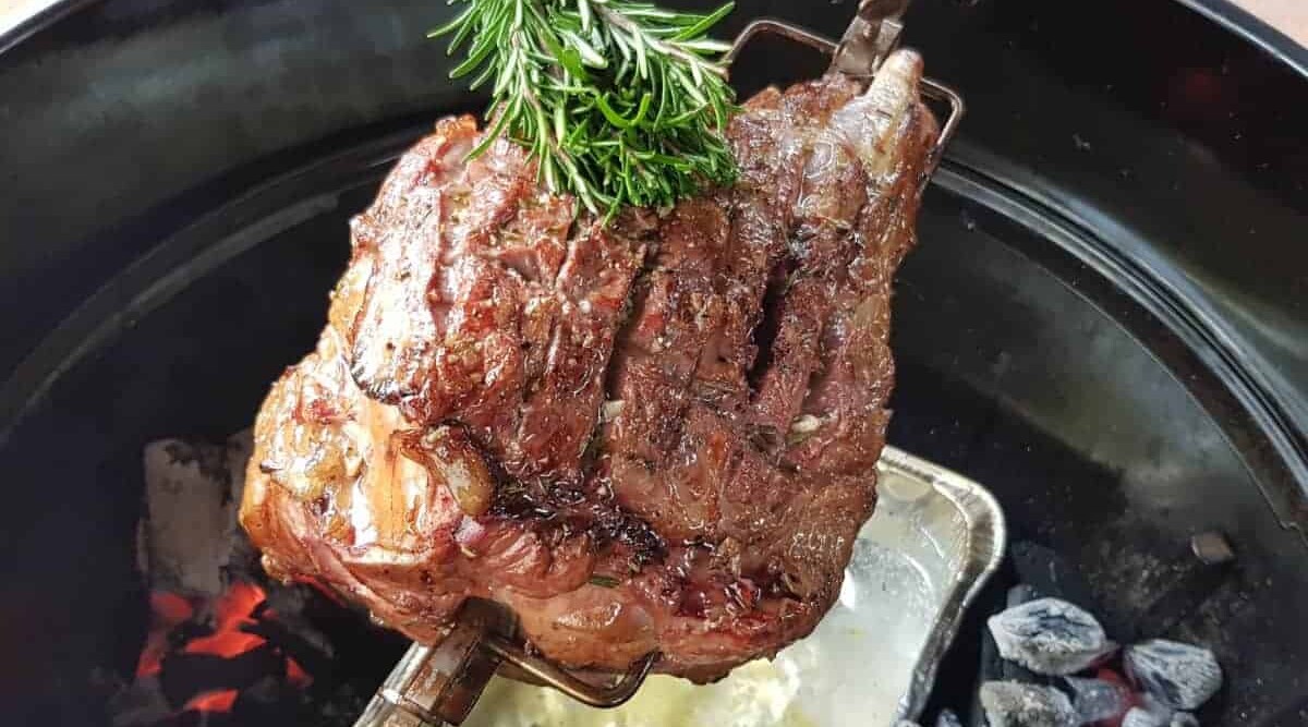 A lamb leg spinning over a wtaer pan, being brushed with a herb brush.