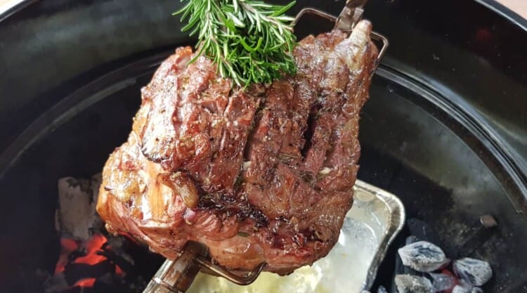 A lamb leg spinning over a wtaer pan, being brushed with a herb brush.