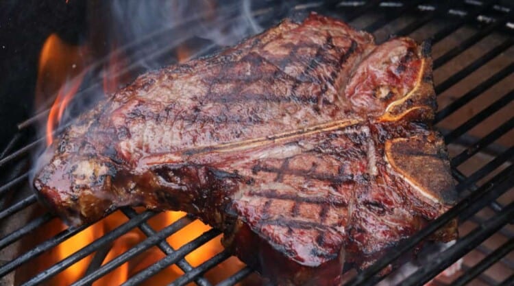 A nicely seared t-bone steak on a charcoal grill.