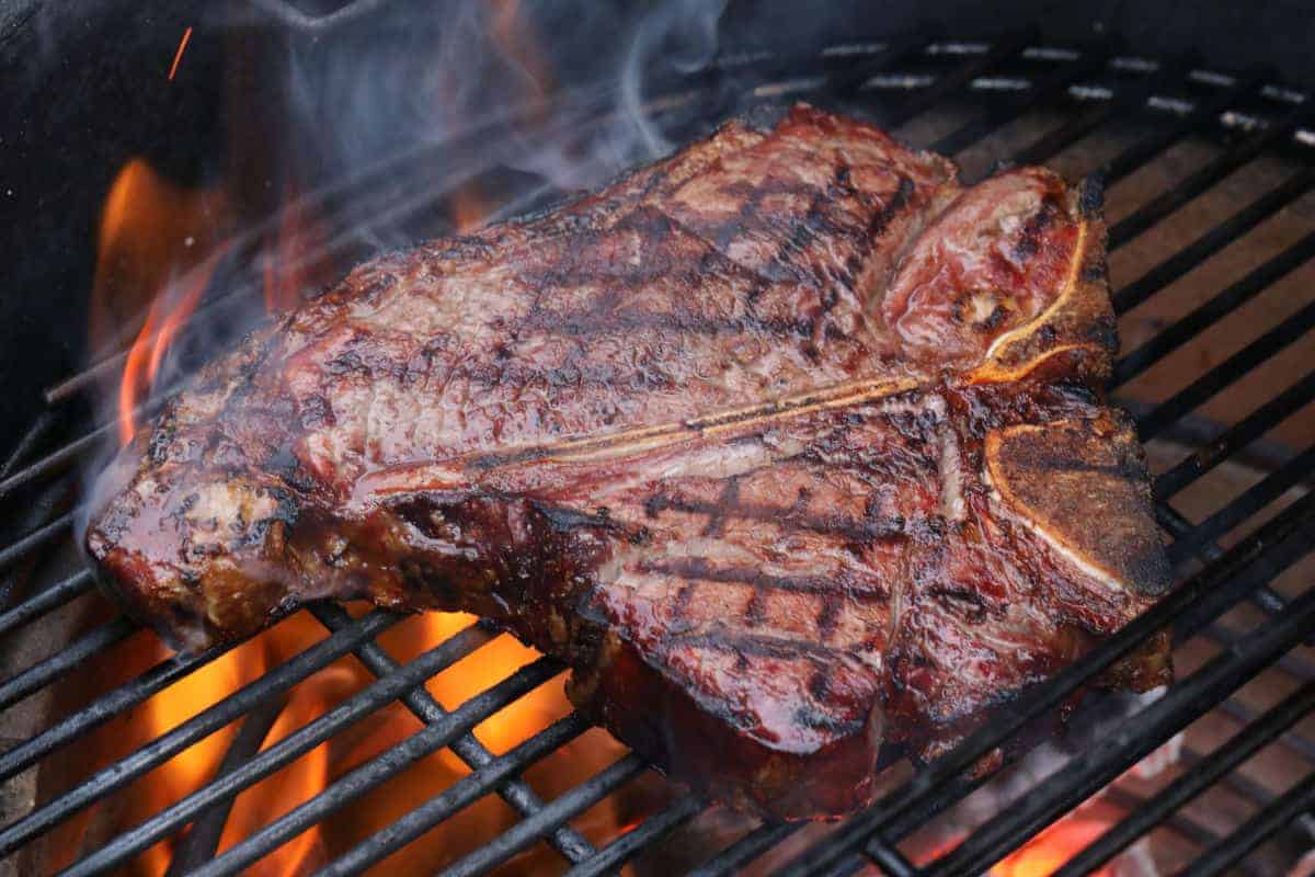 A nicely seared t-bone steak on a charcoal gr.