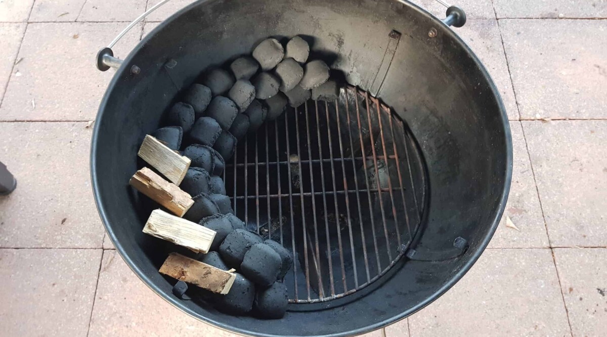 Overhead view of charcoal snake set up in a weber kettle grill with smoking wood on the snake.
