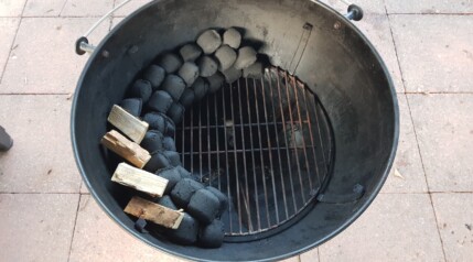 Overhead view of charcoal snake set up in a weber kettle grill with smoking wood on the snake.