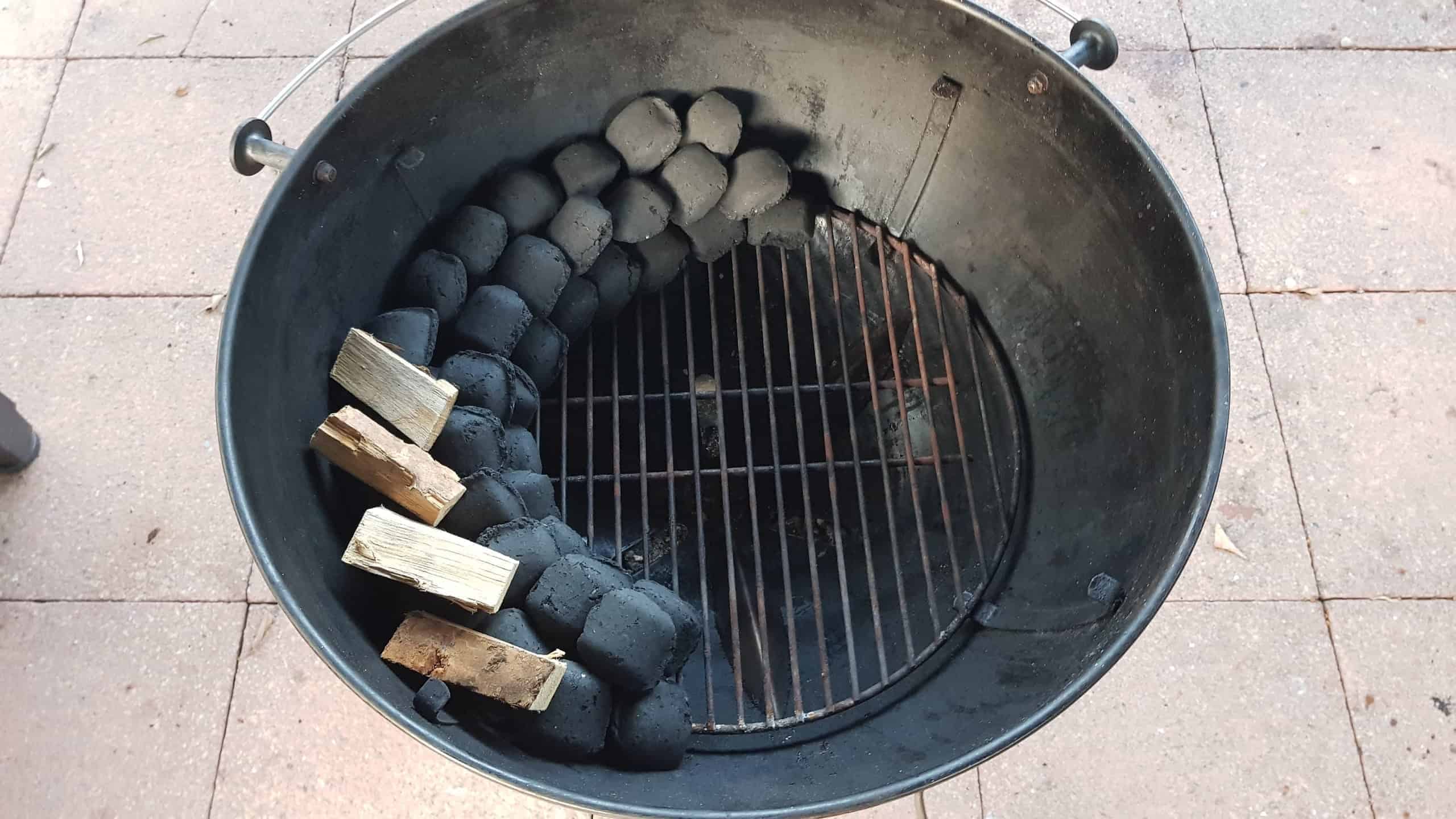 Overhead view of charcoal snake set up in a weber kettle grill with smoking wood on the sn.