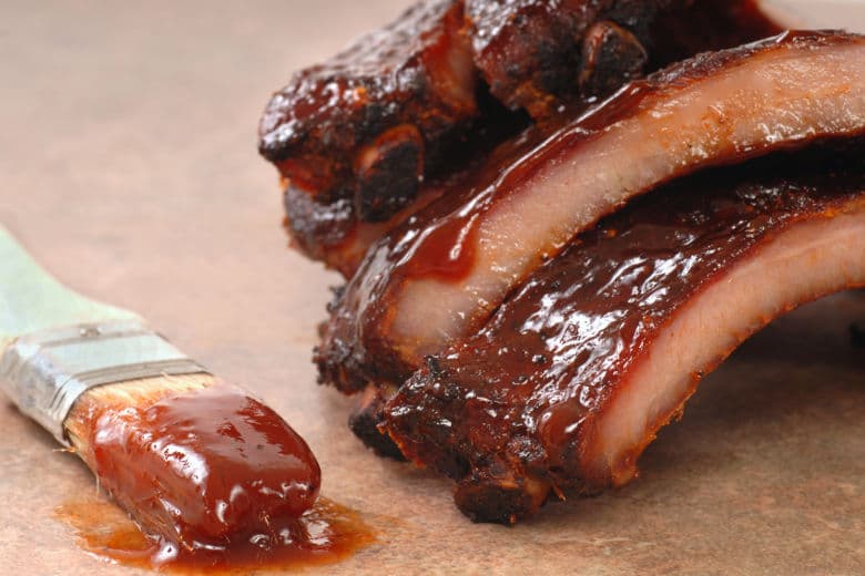 BBQ ribs dripping in thick sauce with a paint brush laying beside them