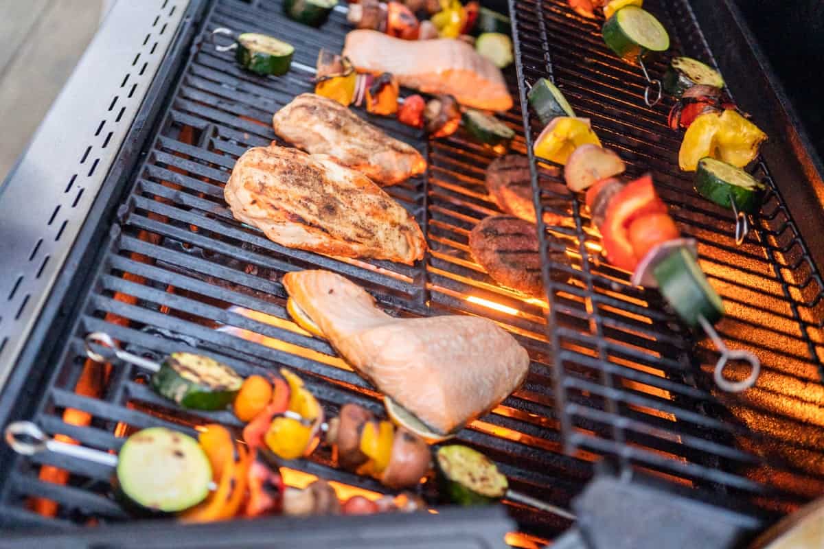 Atlantic salmon, chicken breast, vegetable skewers, and veggie burgers on a flaming gas grill.