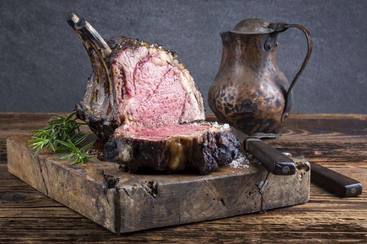 A barbecue prime rib n a chopping block with an antique metal jug and a knife