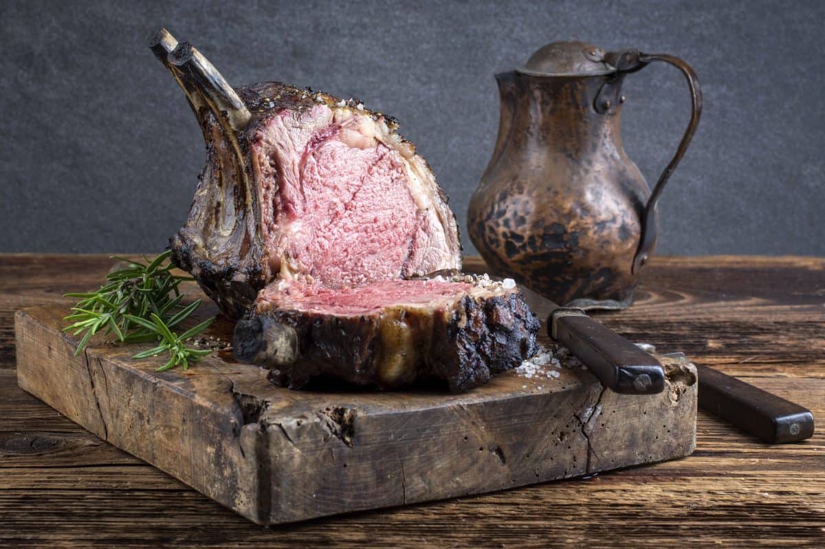 A barbecue prime rib n a chopping block with an antique metal jug and a kn.