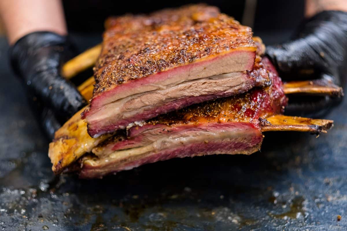 Slow cooked beef ribs sliced in half and held by a man in black glo.