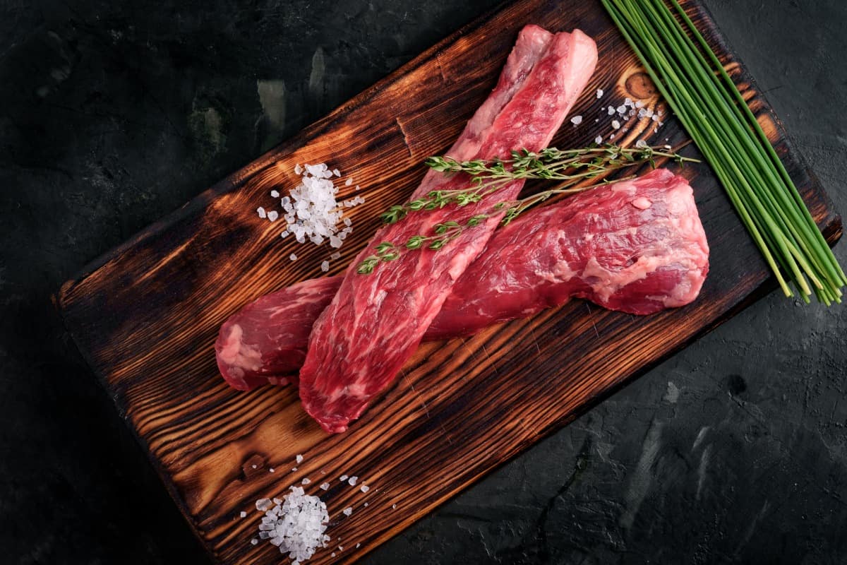 Two beef tenderloin on a cutting board, with sea salt, thyme and unchopped chive stalks