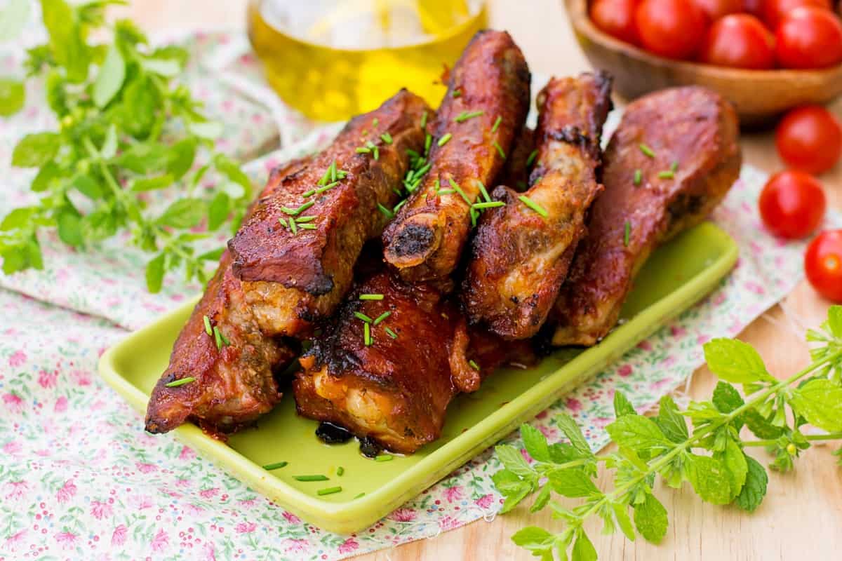 Barbecued country style pork ribs on a green plate and some lettuce and oil around it.