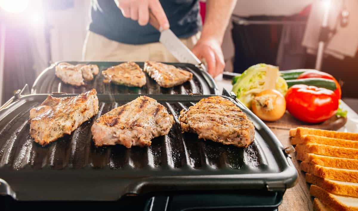 An electric, George Foreman style grill, cooking steaks in a kitc.