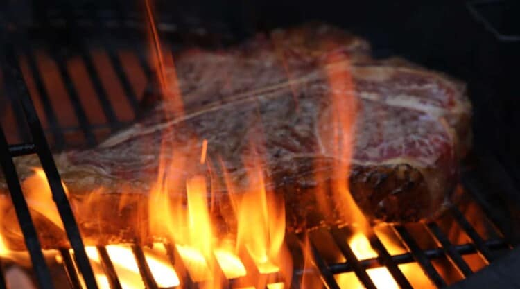 A grill flare up with large flames building under a steak.