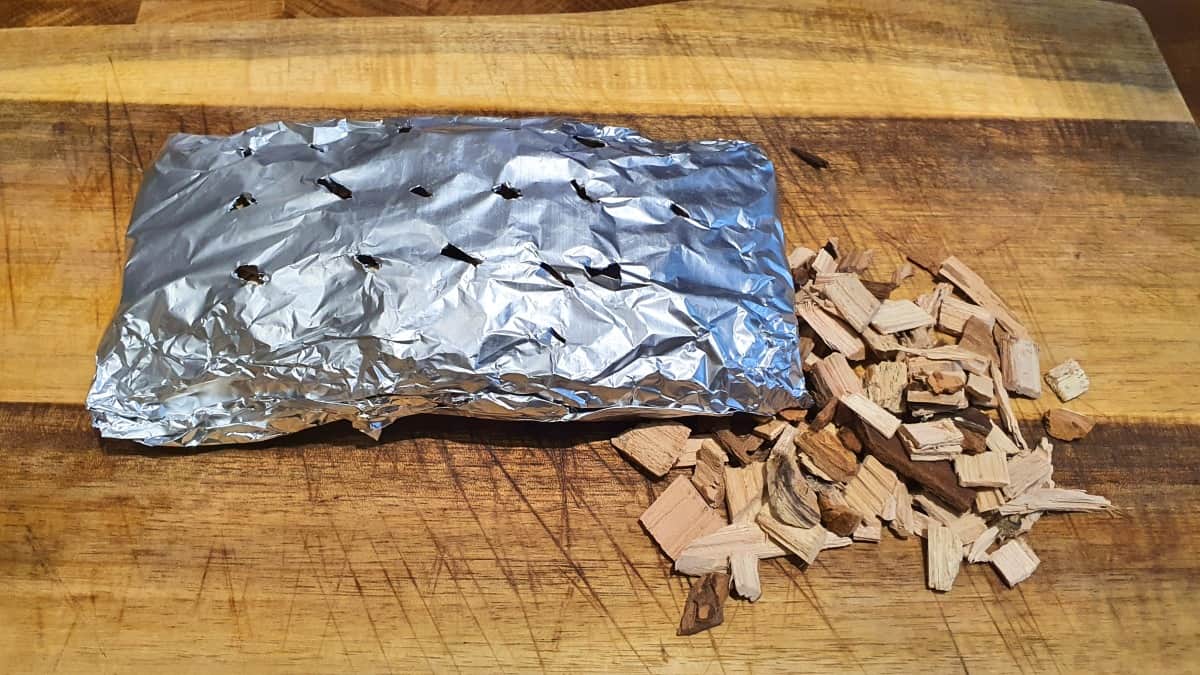 A homemade foil packet for smoking wood chips in a gr.