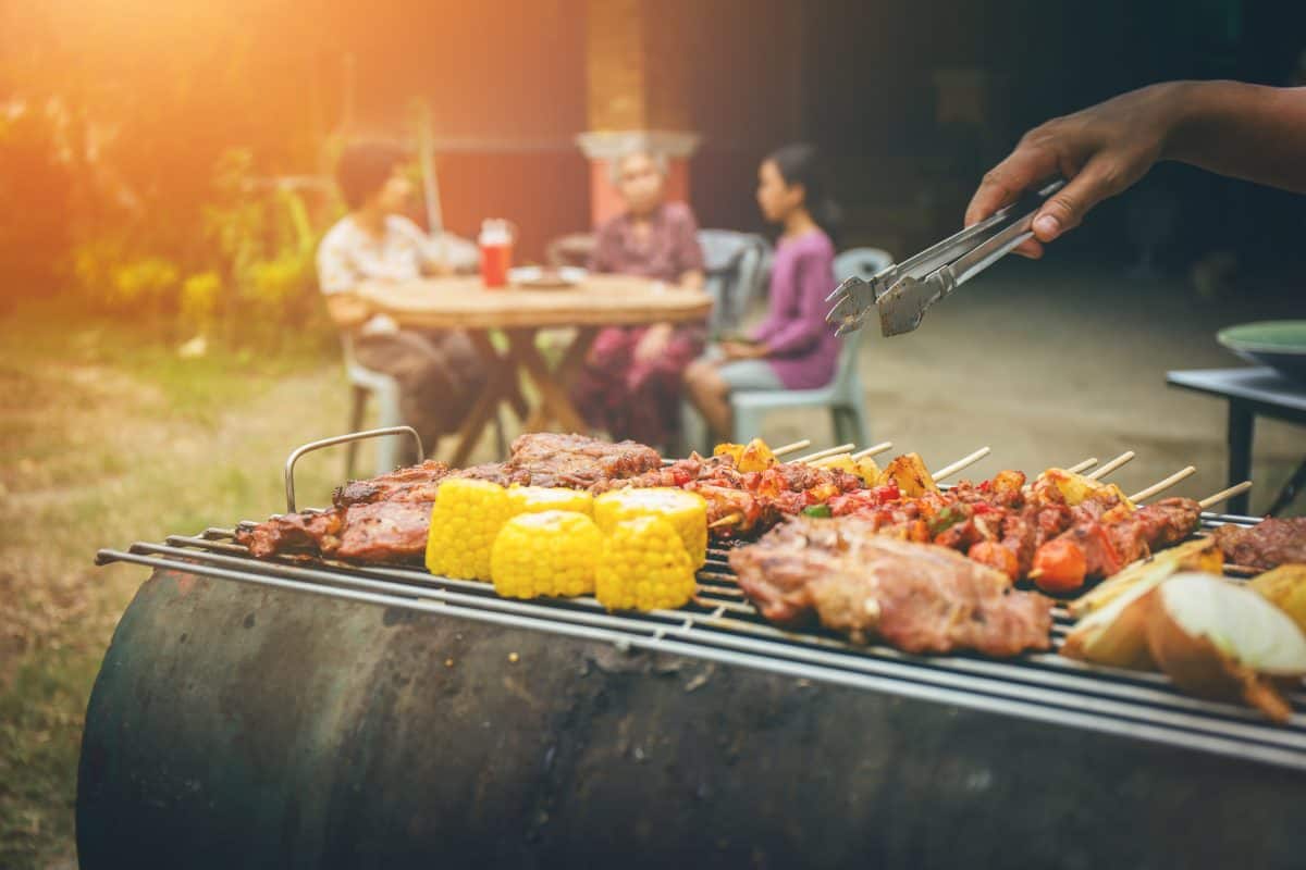 Kebabs, chicken and corn on a grill, with a family at an out of focus table in the backgro.