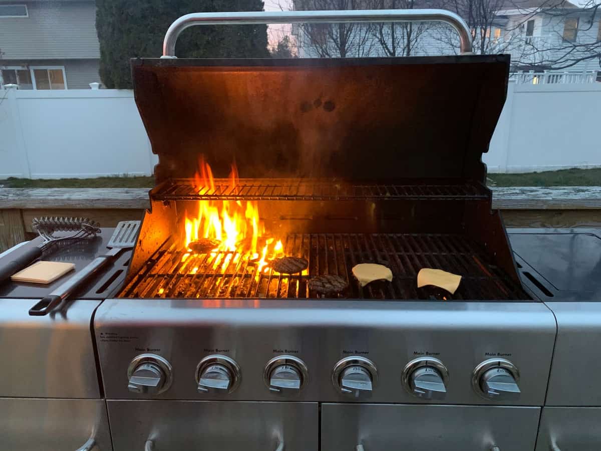 A small fire in a gas grill being used to cook burgers